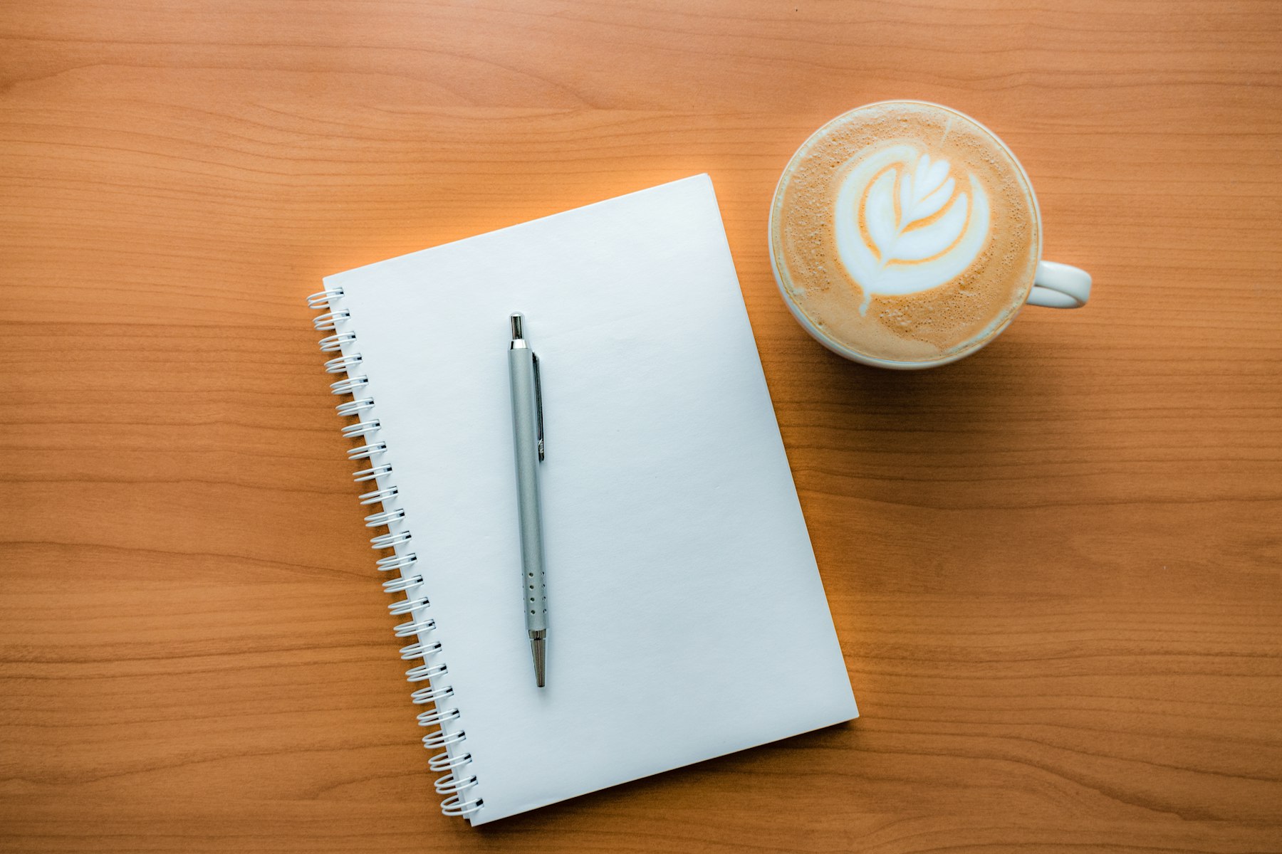 Open notebook and pen beside a latte on a wooden desk