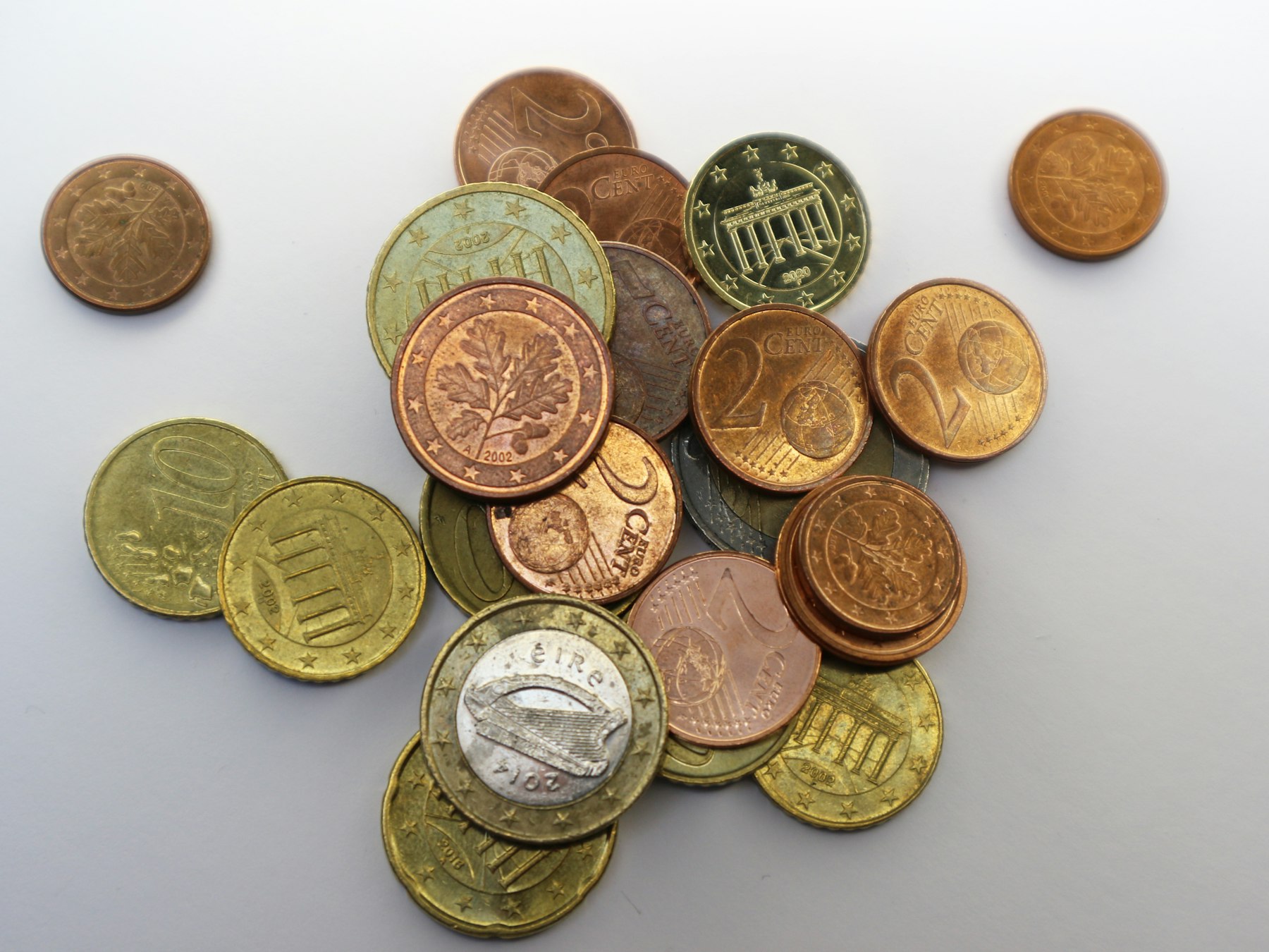Euro coins on a white surface, including an Irish harp one-euro coin