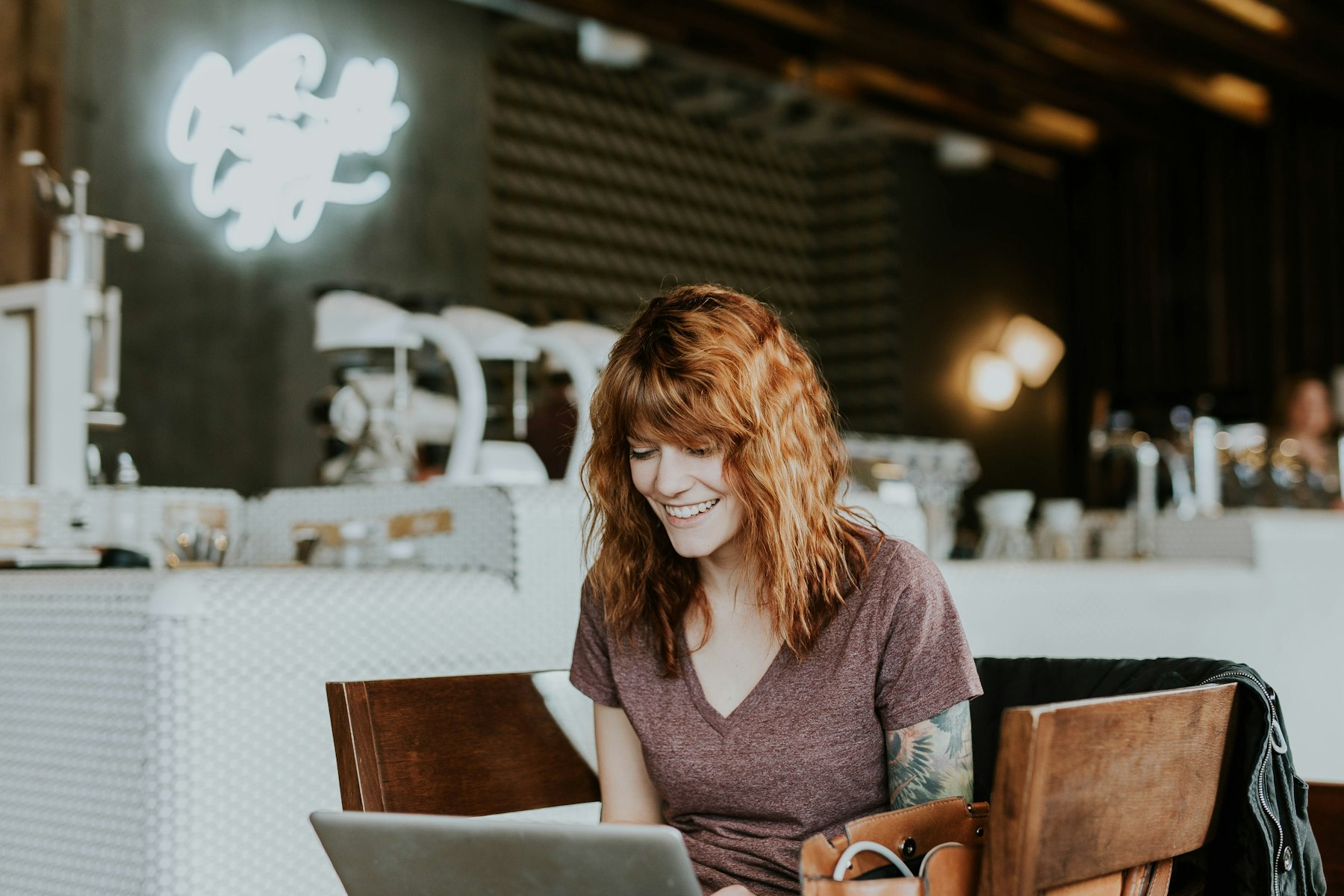 Woman smiling as she works on a laptop in a bright café