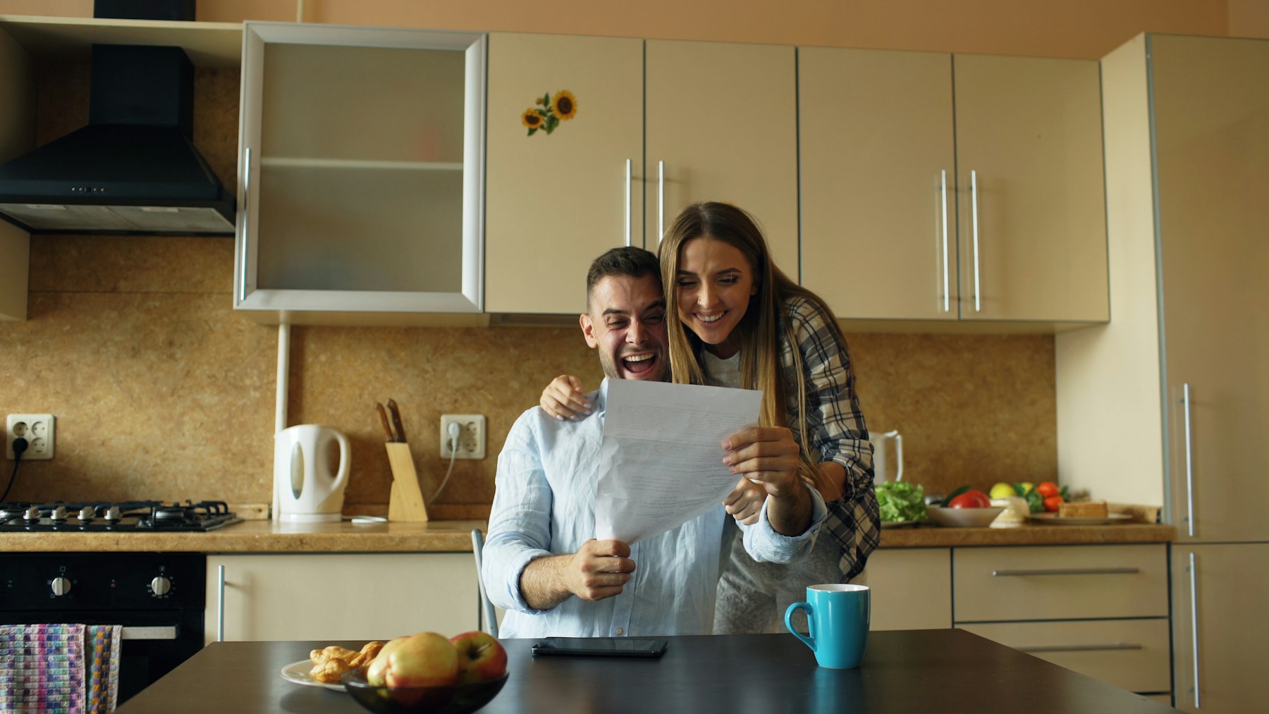 Couple laughing together while reading a letter at their kitchen counter