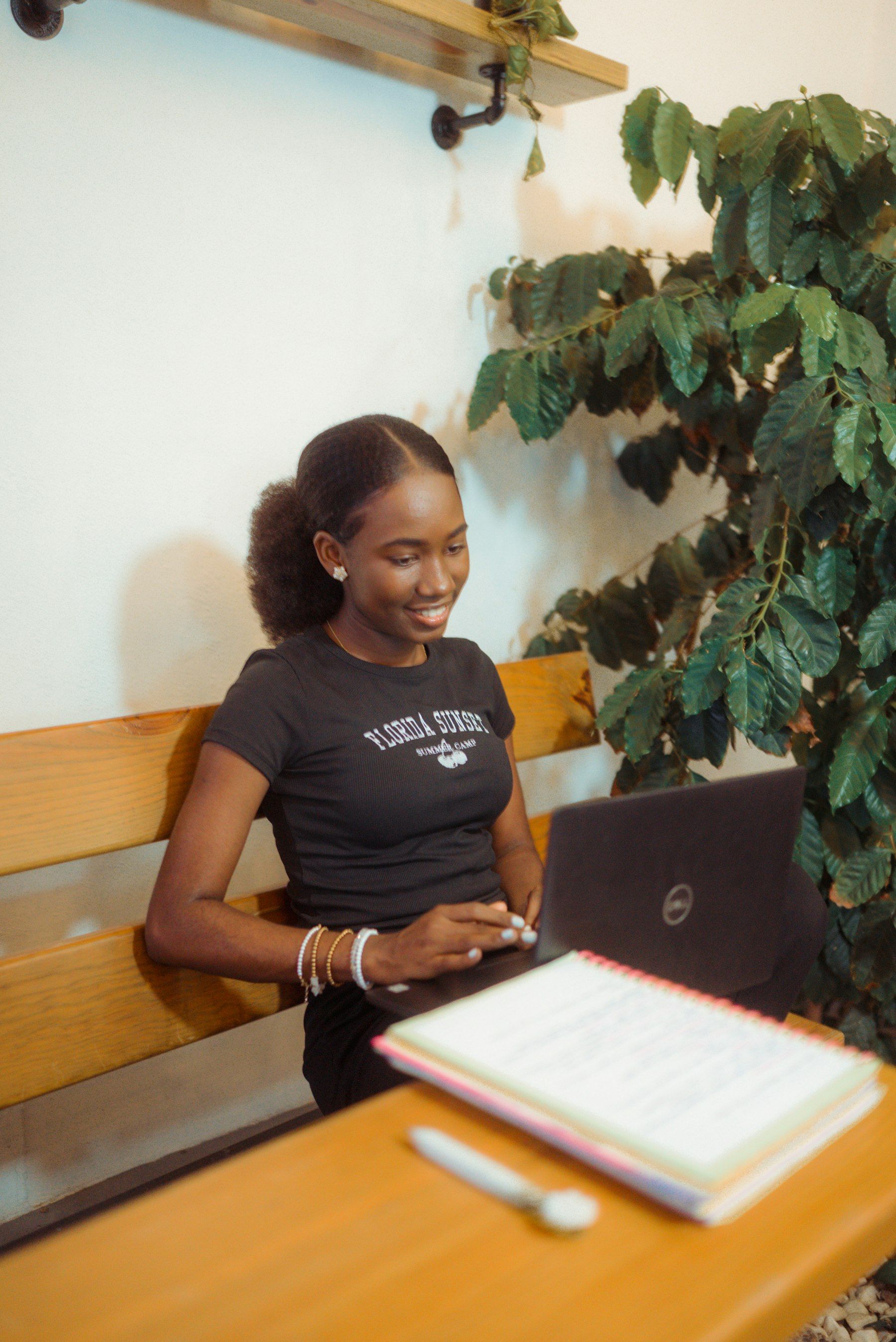 Young woman smiling while working on her laptop at home beside a houseplant