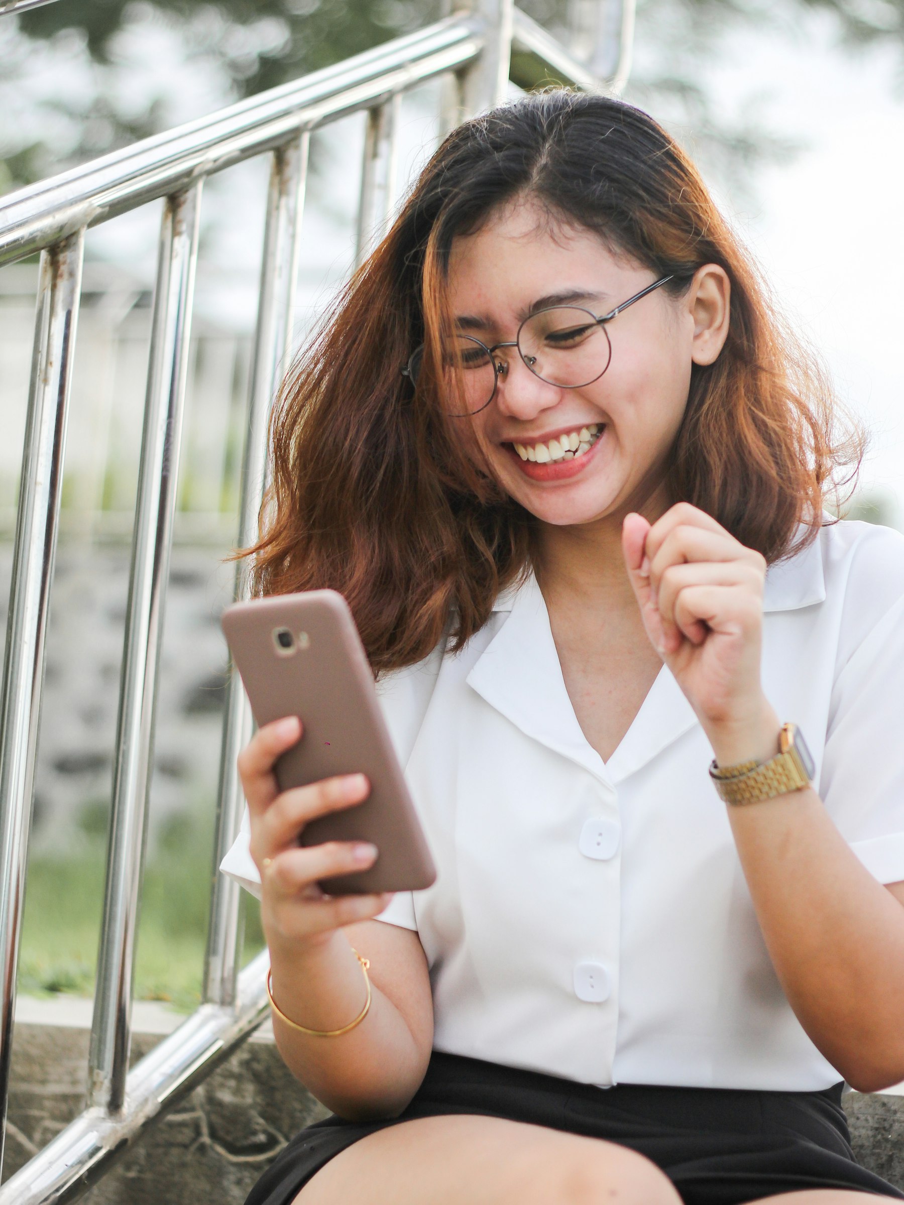 Young woman in glasses smiling as she reads good news on her phone