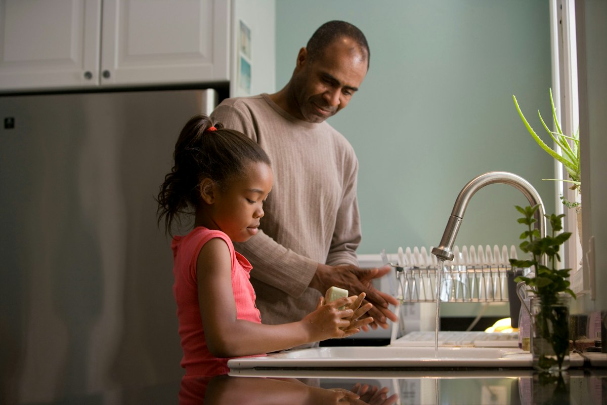 Father and young daughter washing up together at the kitchen sink